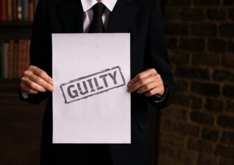 A businessman in a formal suit holding a sign with the word 'GUILTY.'