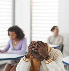 Young man stressed during an exam in a classroom setting.