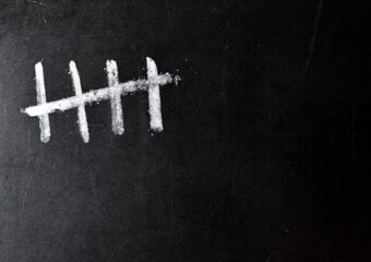 Five chalk tally marks on a black chalkboard; counts background.